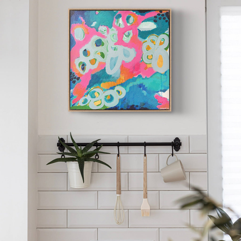 Colorful abstract painting on a wall above a kitchen with white tiles and wooden bench.