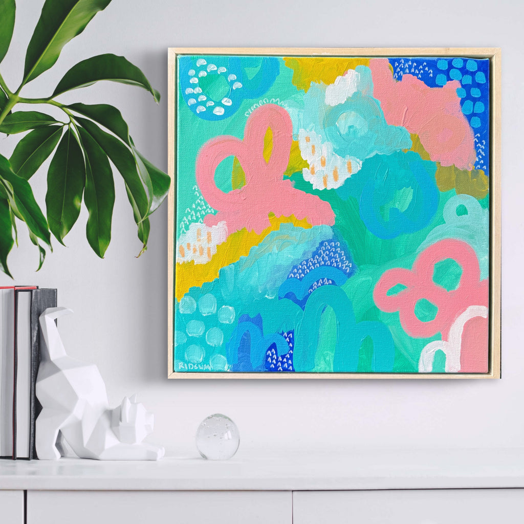 Colorful abstract painting on a wall above a white cabinet with books and decor items.